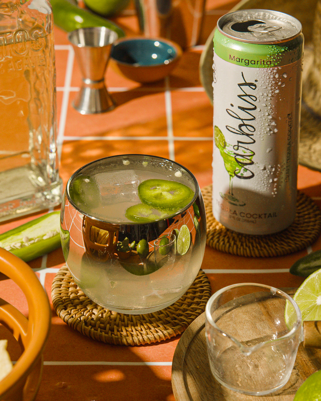 Cocktail with lime slices in a glass next to a can of Caribliss margarita mix on a table.