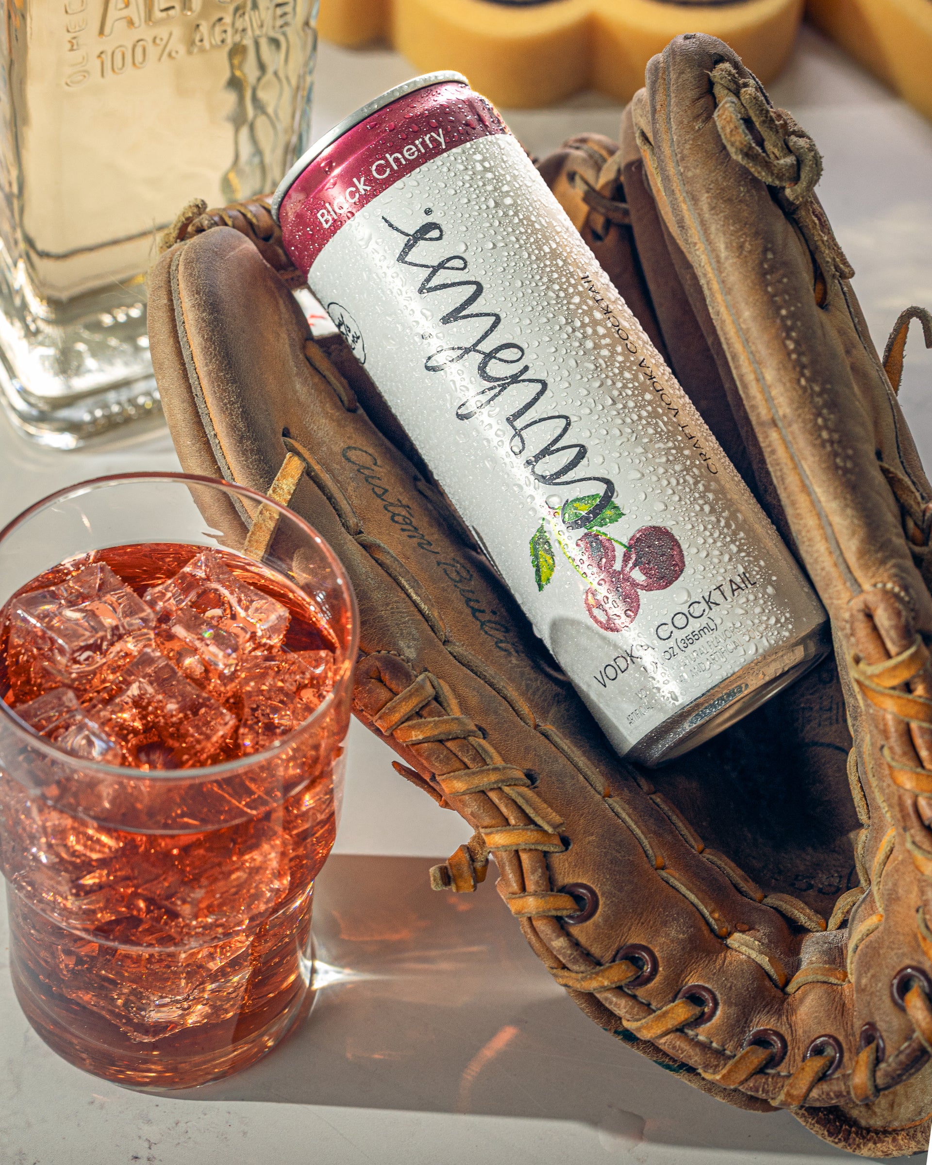Canned cocktail in a glove with a glass of red liquid on a white surface