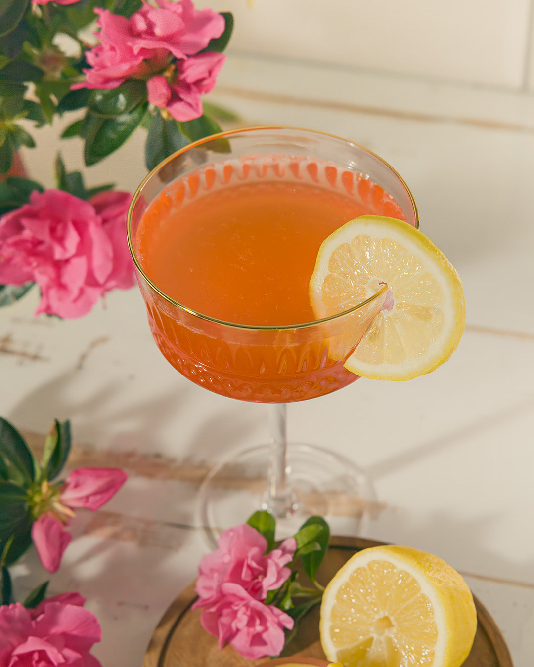 Cocktail with a lemon wedge and pink flowers on a light background