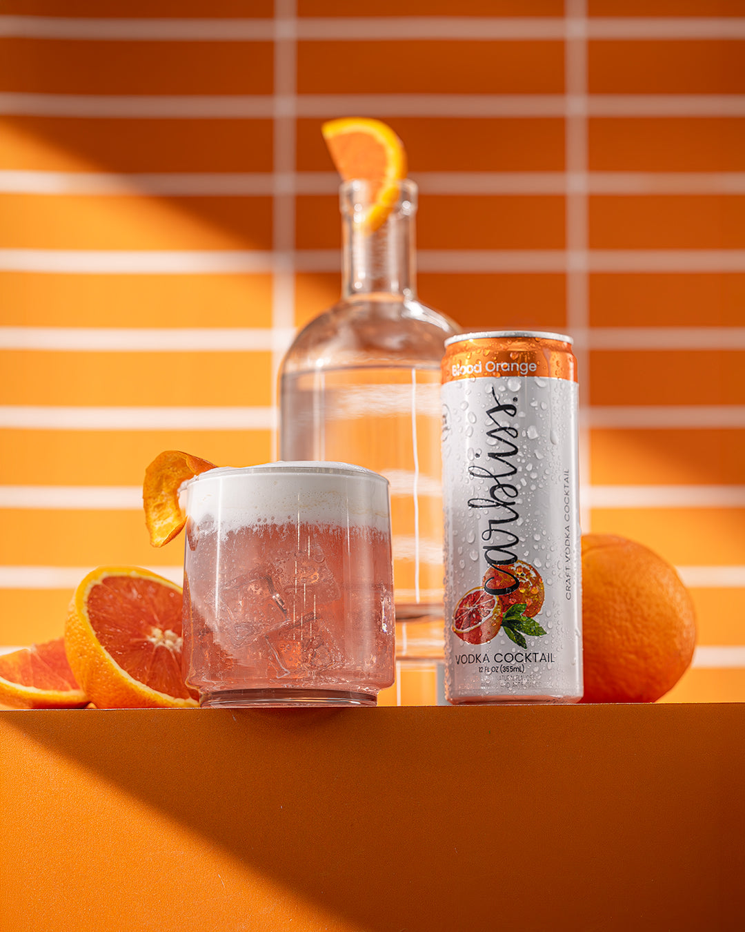 Vodka bottle, can of cocktail, and glass with orange slices on an orange striped background
